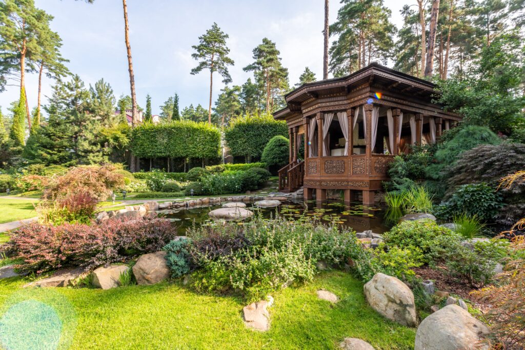 A peaceful garden pavilion beside a pond surrounded by trees and greenery