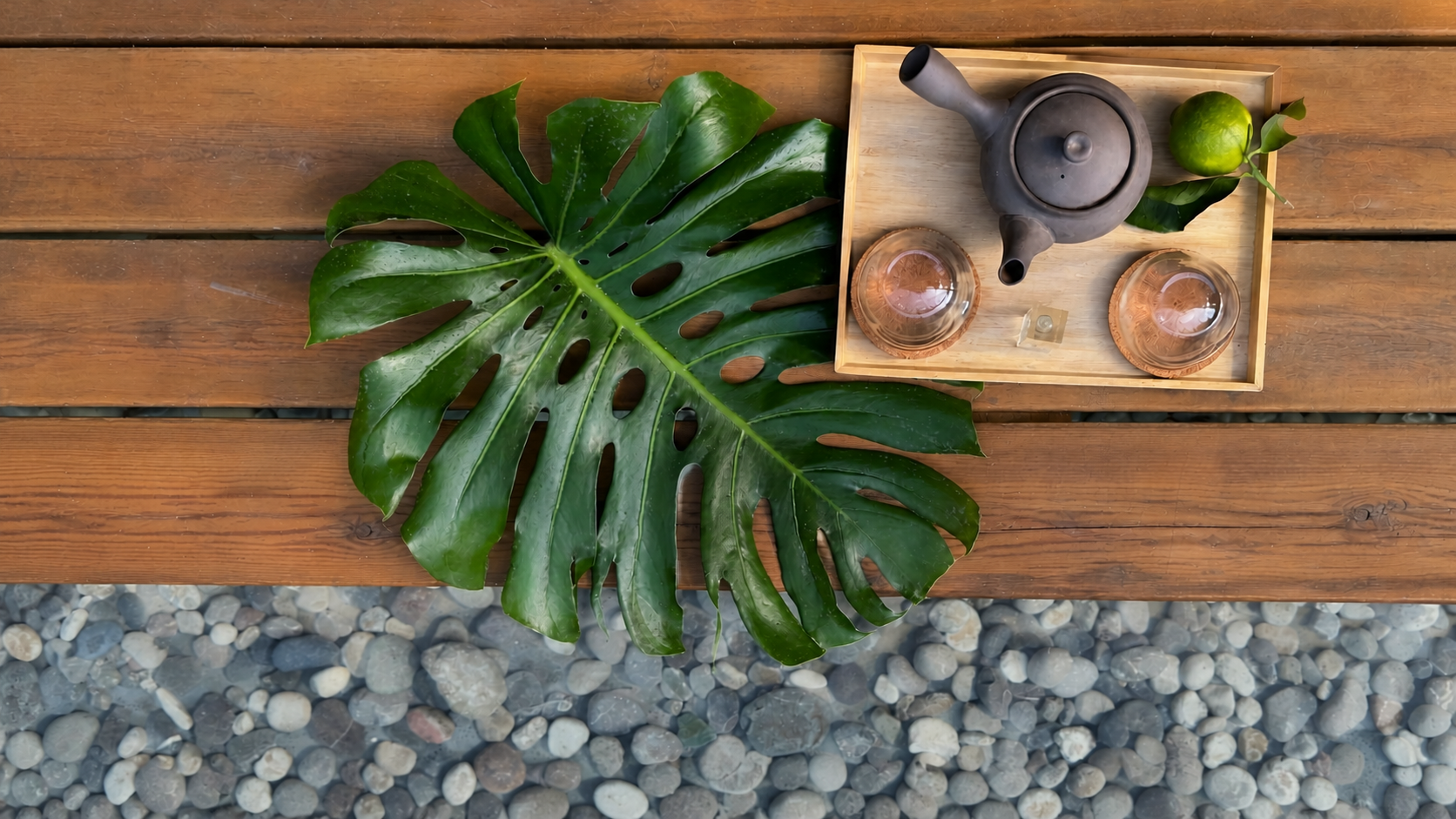 Tea ritual with a ceramic teapot, monstera leaf, warm wood, and smooth stones